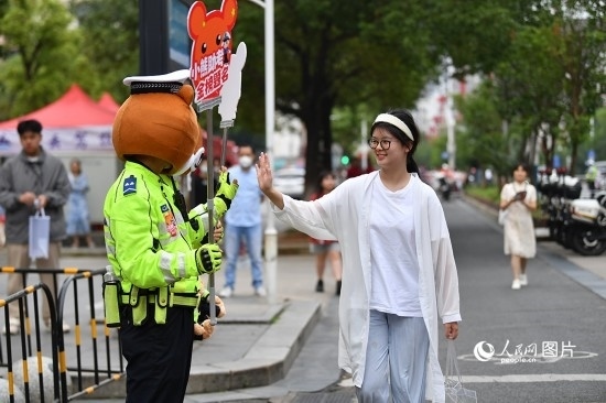 6月7日上午9時(shí)，隨著鈴聲的響起，2023年江西高考正式開考，江西省的53.57萬考生以縣（區(qū)）為單位隨機(jī)安排在全省256個考點(diǎn)、18968個考場參加高考。圖為“小熊交警”和考生擊掌鼓勵。 人民網(wǎng)記者 時(shí)雨攝