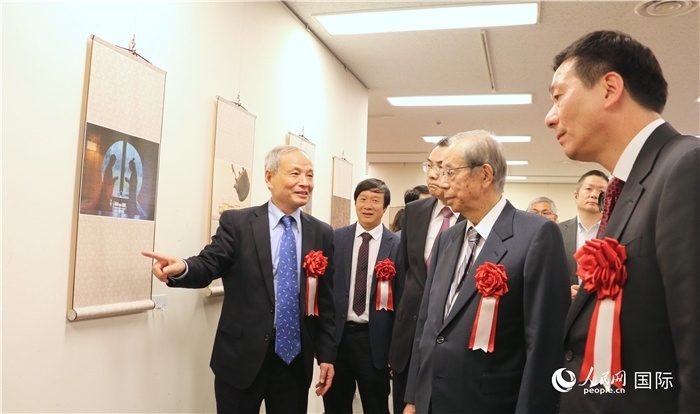 “湖州印象”攝影展主創(chuàng)、世界華人攝影協(xié)會副會長馮學(xué)敏向吳江浩大使、福田康夫前首相等嘉賓介紹展出作品。（人民網(wǎng) 許可攝）