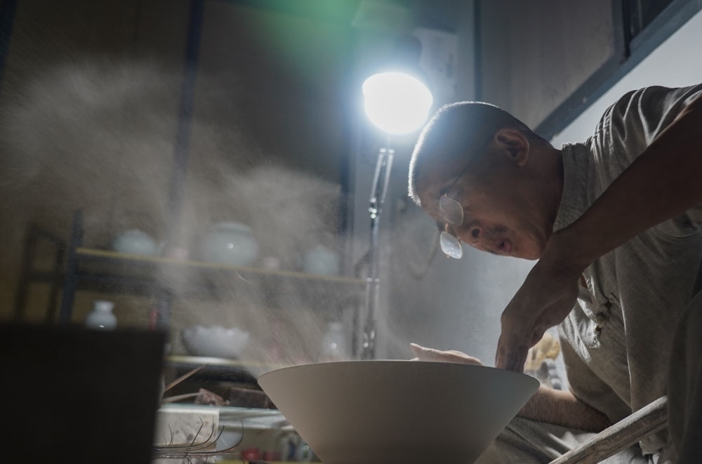 ↑ 在景德鎮(zhèn)，手工匠人吹去坯內(nèi)的泥土（2021年7月14日攝）。