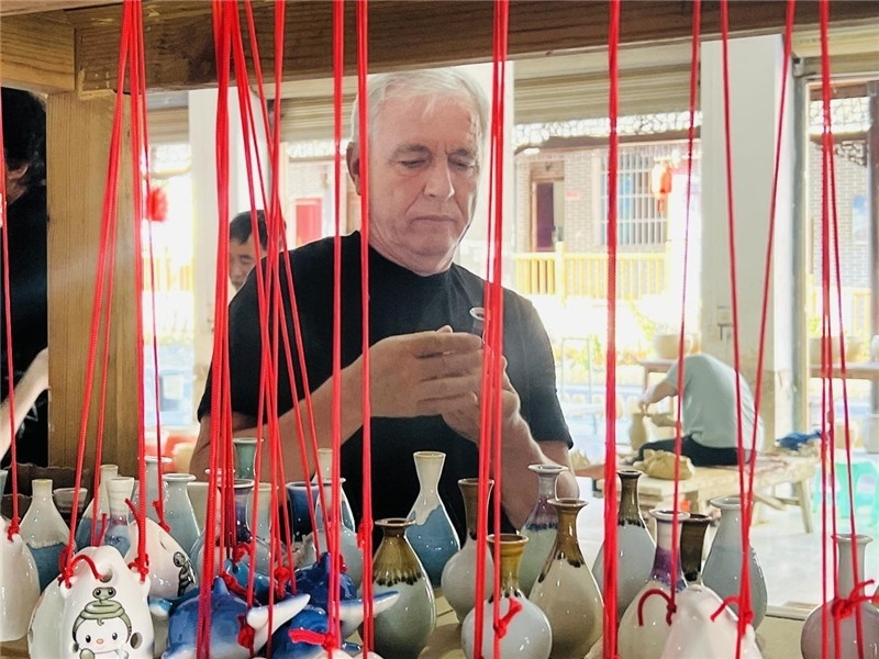 鄉(xiāng)愁如同一根根紅線，將游子與故鄉(xiāng)永遠(yuǎn)地牽連到一起。花茂村陶藝文化創(chuàng)意一條街的母氏陶藝館內(nèi)，紅線吊著陶瓶，思緒游走萬里。摩爾多瓦“信息標(biāo)簽”通訊社社長亞歷山大·塔納斯端詳著館內(nèi)展示的陶藝作品，并挑選出心儀的小擺件帶回摩爾多瓦，也帶走花茂村的“鄉(xiāng)愁”。（張亞欣攝）